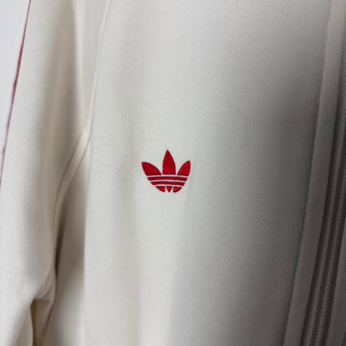 Detalhe do logo Adidas Trefoil vermelho no peito da jaqueta
