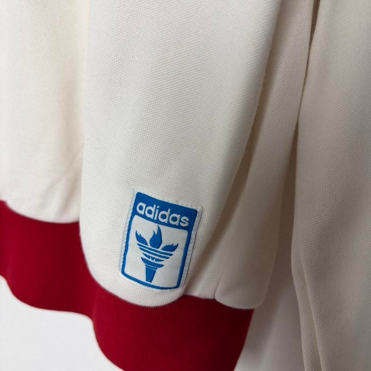Detalhe da etiqueta azul Adidas e da barra vermelha da jaqueta