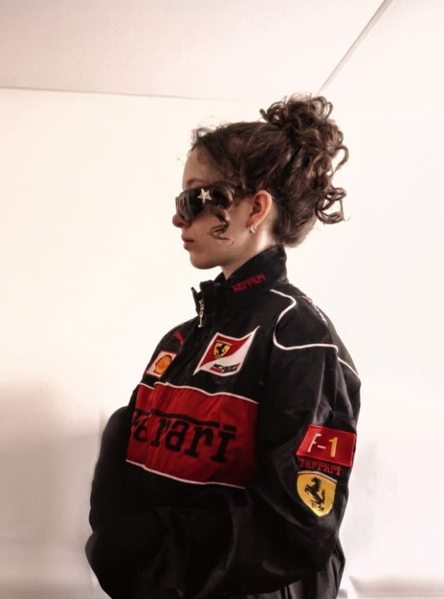 Jaqueta Ferrari preta e vermelha, de perfil, com óculos escuros